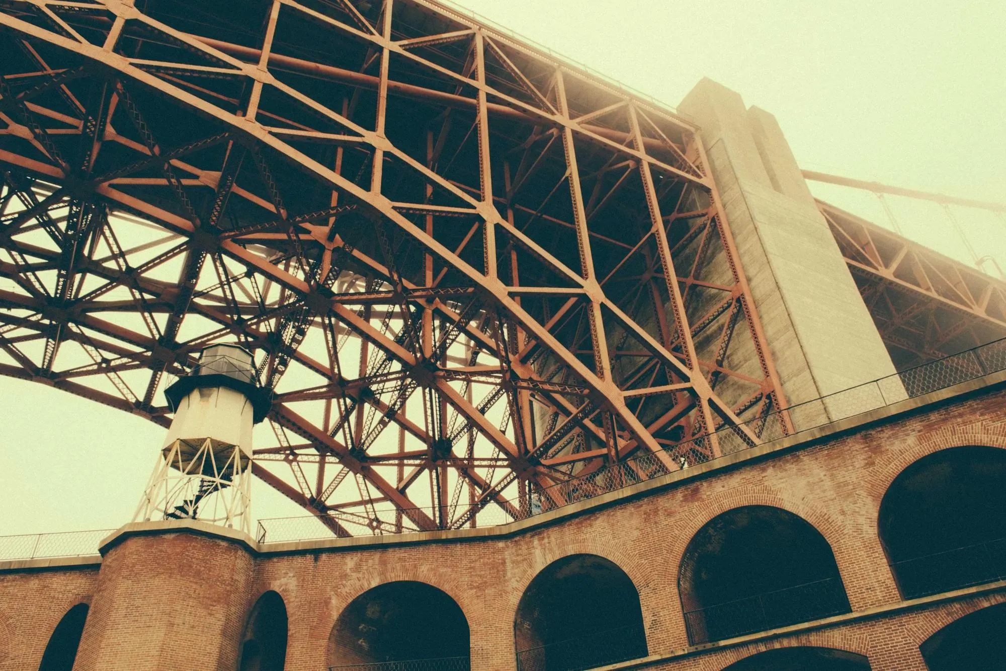 Steel lattice of a bridge seen from below, above a row of brick arches