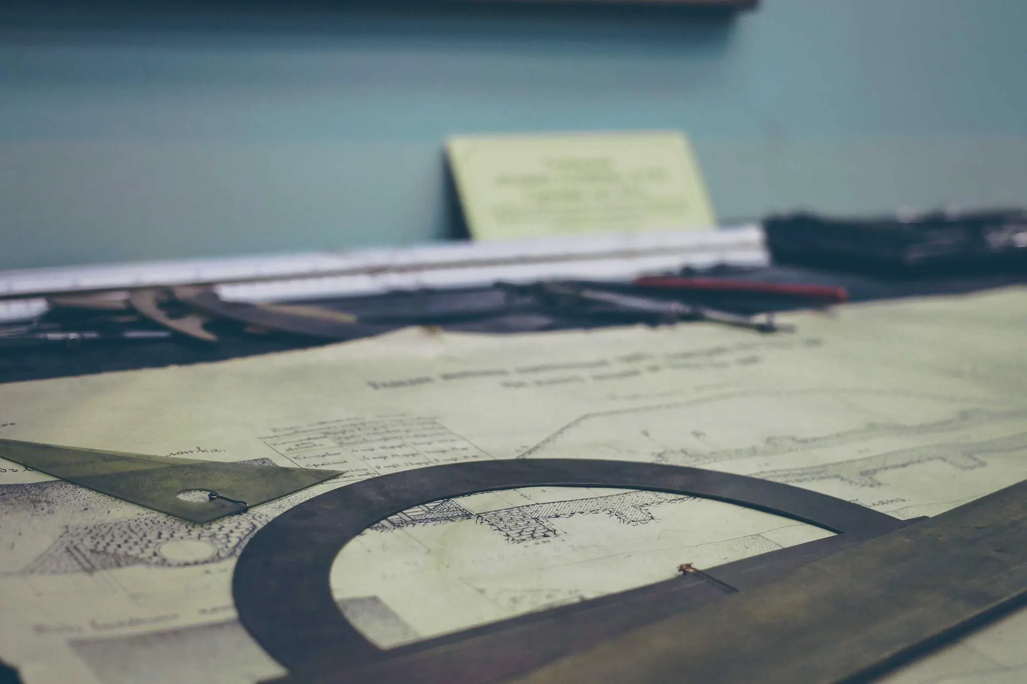Drafting table covered in technical drawings, with a protractor and set square