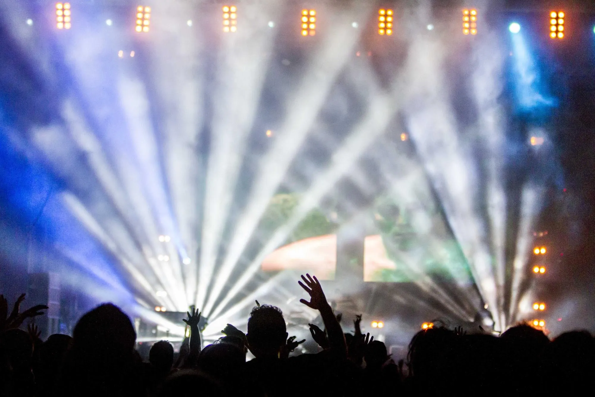 Crowd with raised hands under white stage beams