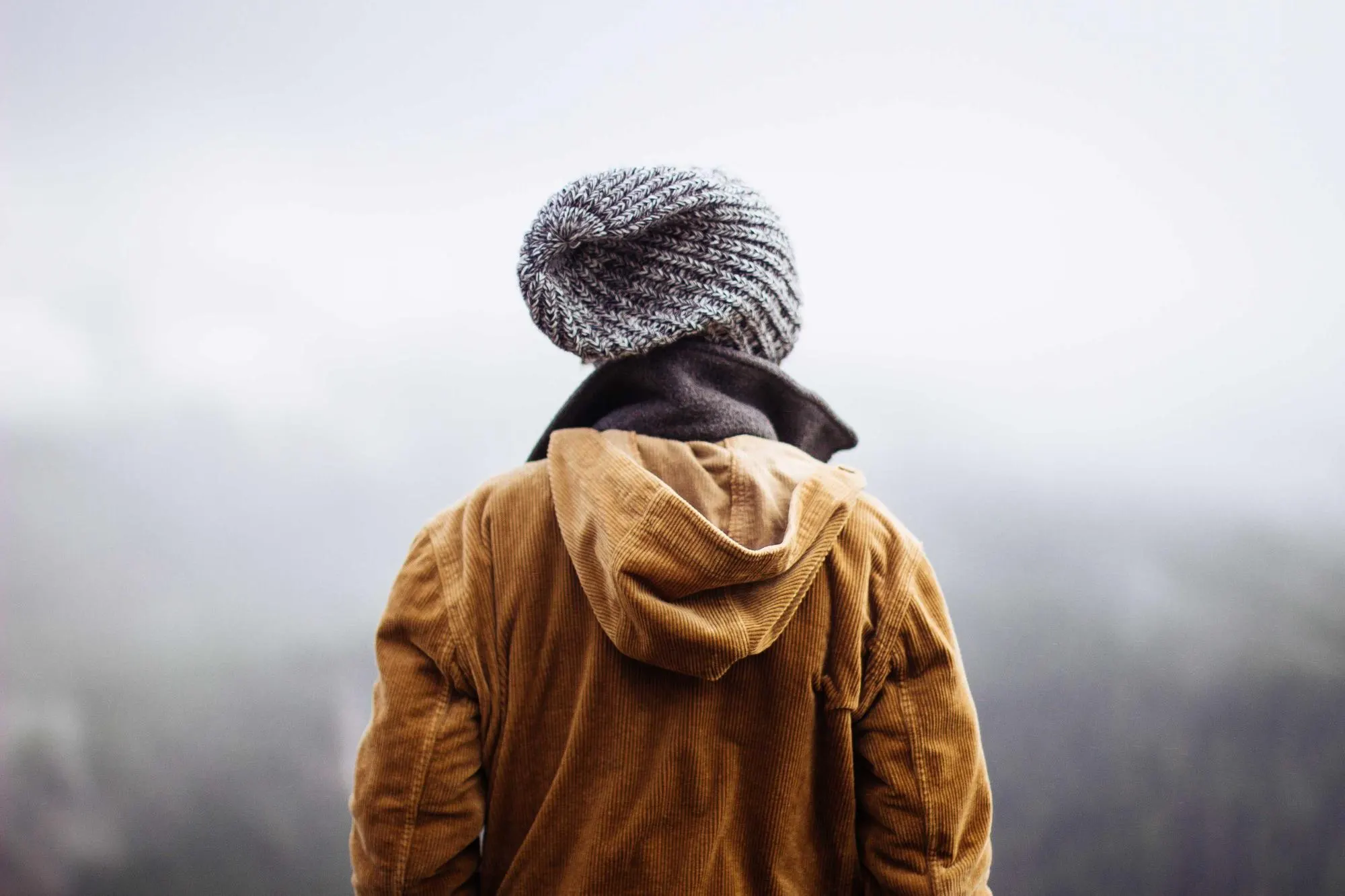 Person in an orange jacket and knitted hat facing a misty horizon