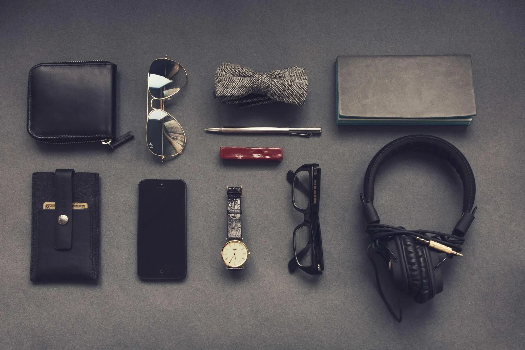 Flat lay of headphones, watch, glasses and notebook on grey fabric