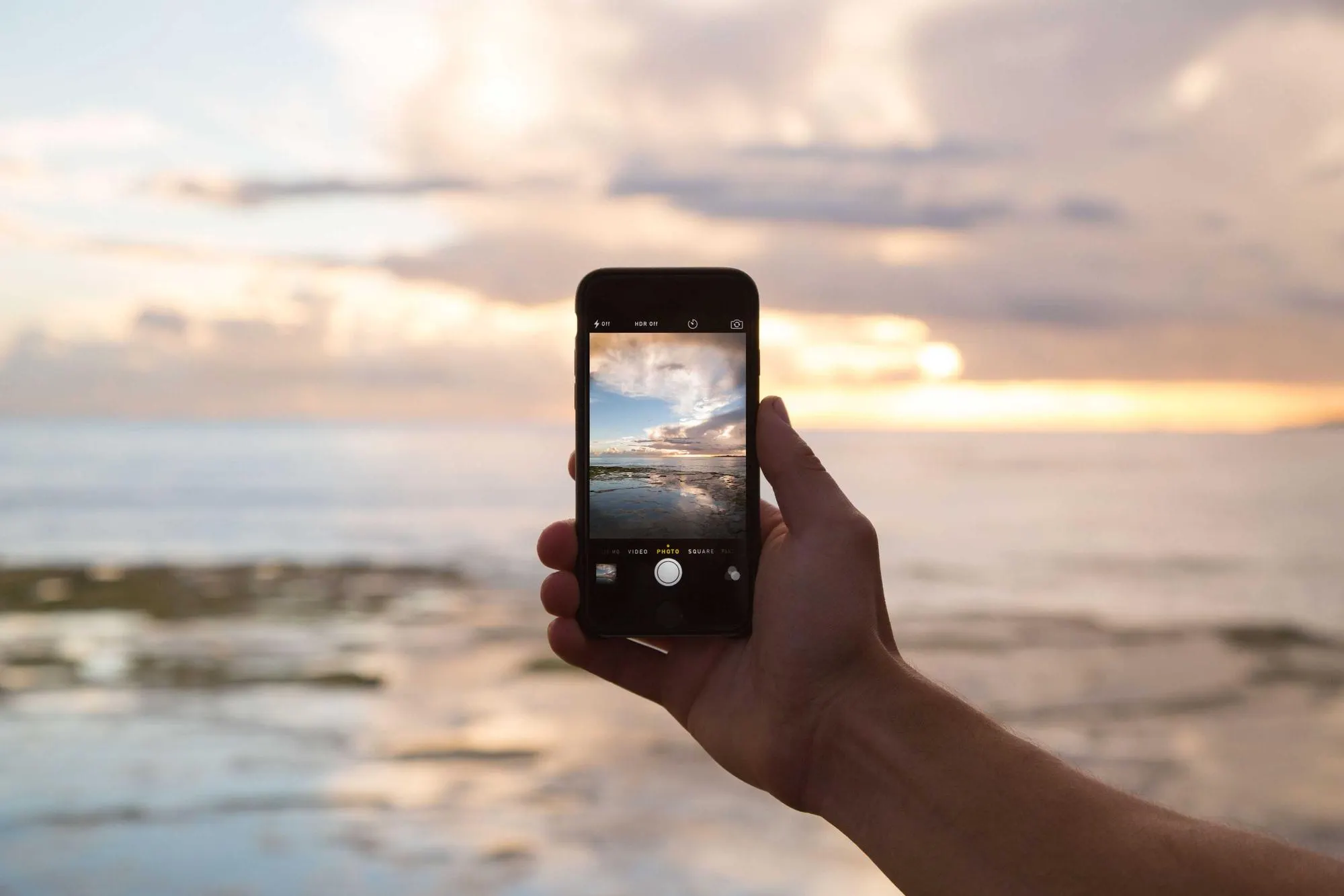 Hand holding a phone up against the sea and sky